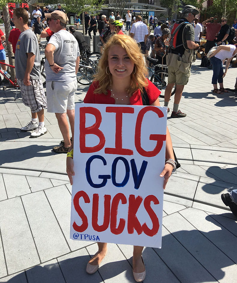 Protester holding a painted sign that reads "Big Gov Sucks (@TPUSA)"